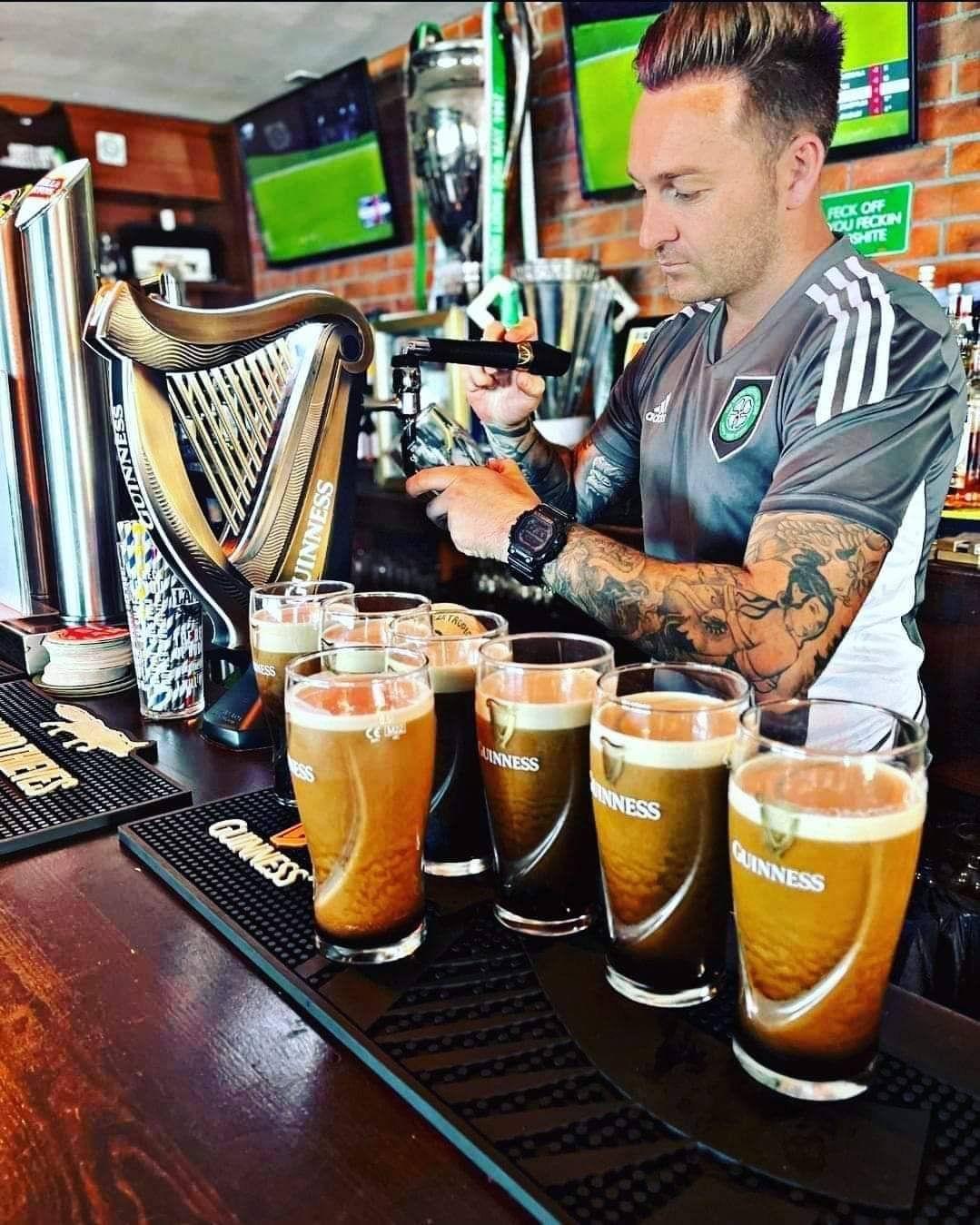 Wayne Murphy pouring a line of pints of Guinness behind the Bar 67 bar in his Celtic shirt